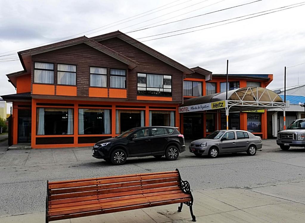 a wooden bench in front of a building with parked cars at Agostini Hotel in Puerto Natales
