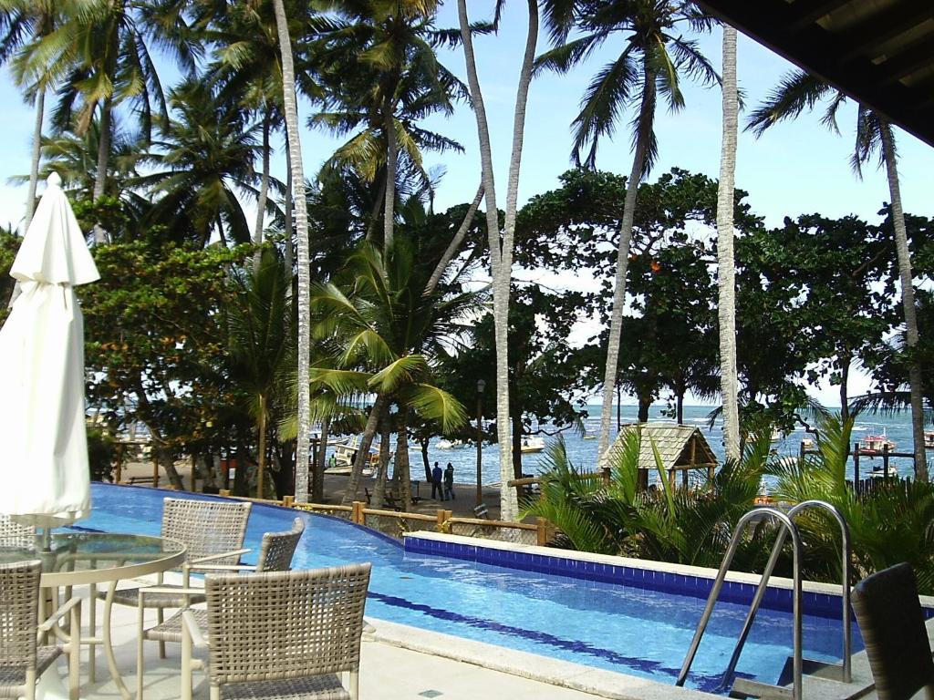 una piscina con mesa, sillas y palmeras en Apartamento Enseada Praia do Forte, en Praia do Forte