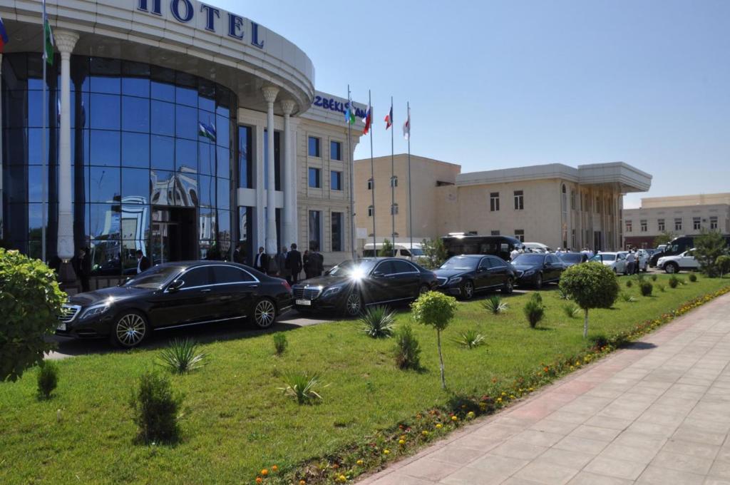 eine Gruppe von Autos, die vor einem Gebäude geparkt sind in der Unterkunft Hotel Uzbekistan in Urganch