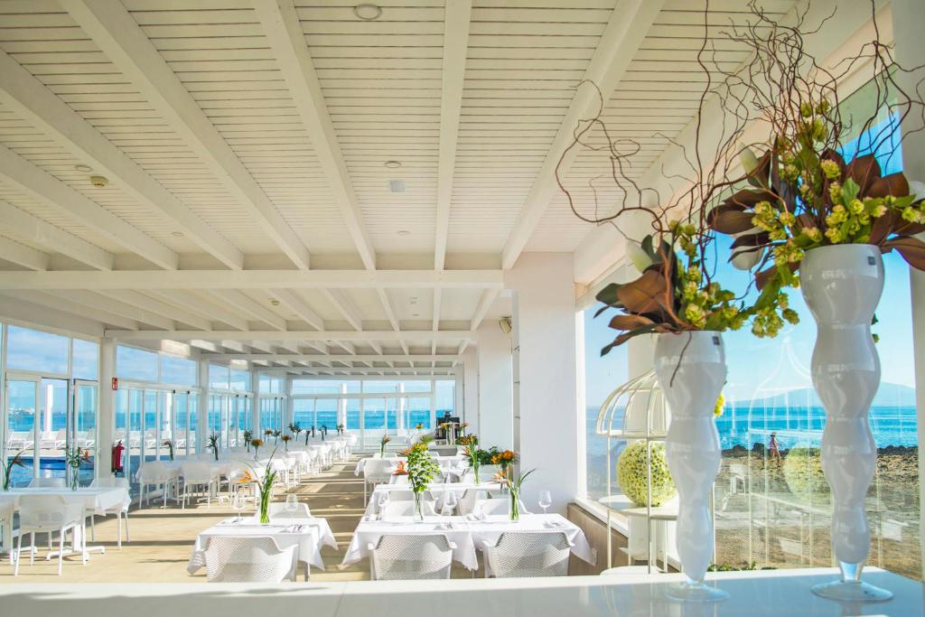 a dining room with white tables and vases with flowers at Hotel Boutique TAO Caleta Mar in Corralejo
