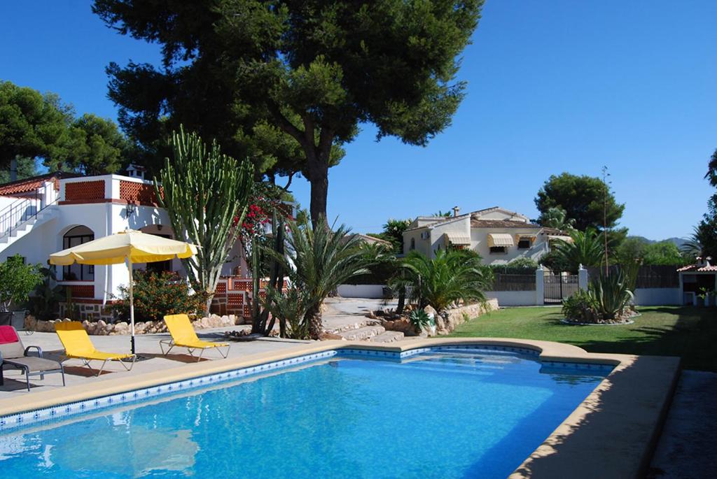 a swimming pool with chairs and an umbrella and a house at Villa Maria Beach Villa in Moraira