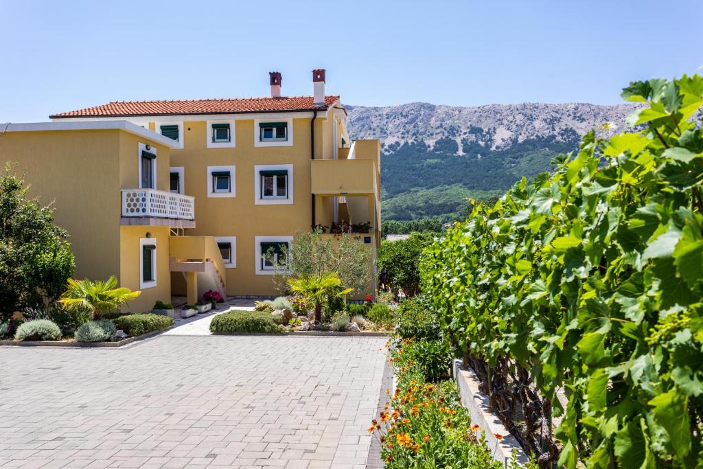 a large yellow house with a brick driveway at Apartments Marija in Baška