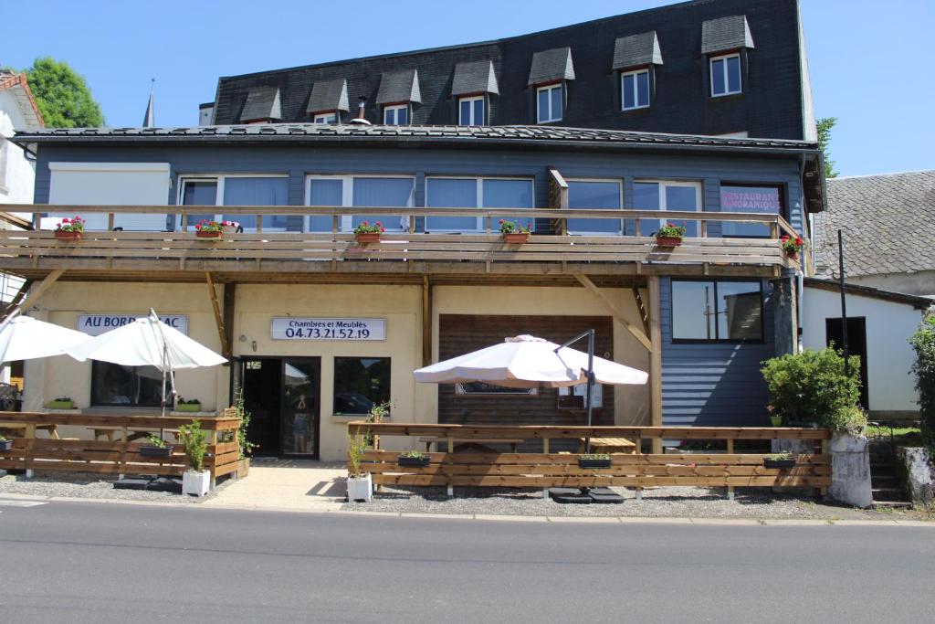 a building with tables and umbrellas in front of it at Hotel du Lac - Au Bord du Lac in La Tour-dʼAuvergne