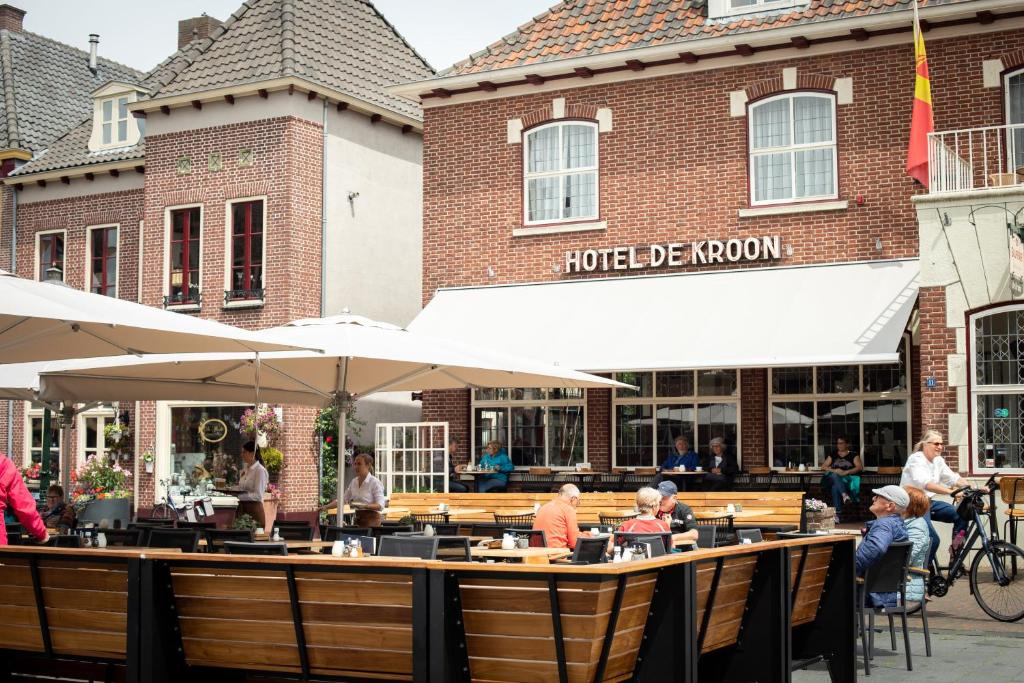 un groupe de personnes assises dans un restaurant avec des parasols dans l'établissement Hotel De Kroon Gennep, à Gennep