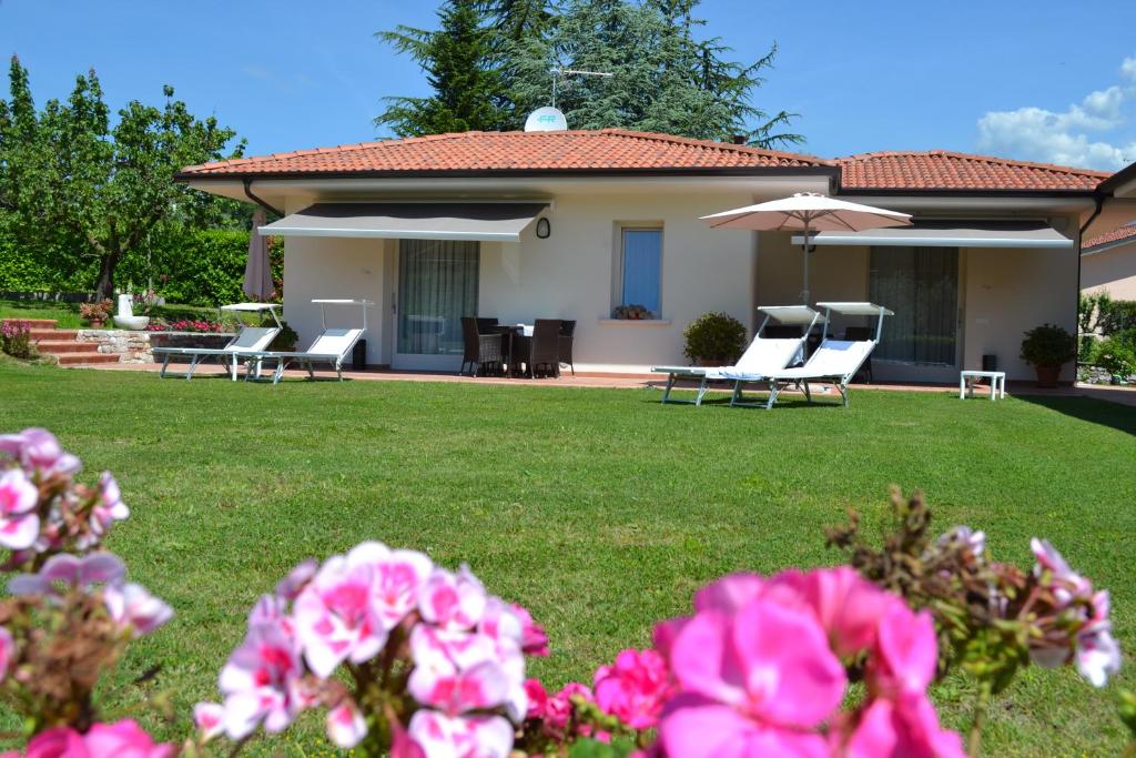 a house with chairs and an umbrella and some pink flowers at Villa Josephine in San Felice del Benaco