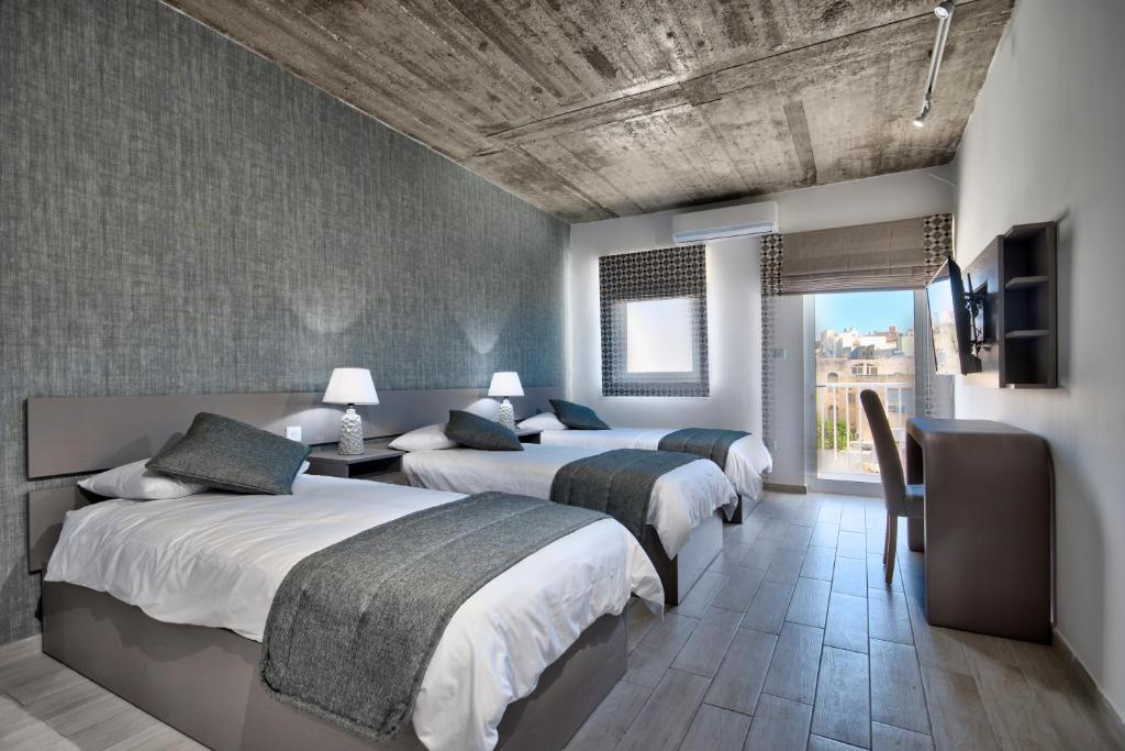 a bedroom with two beds and a tv and a window at Cozy Rooms Hotel in Sliema