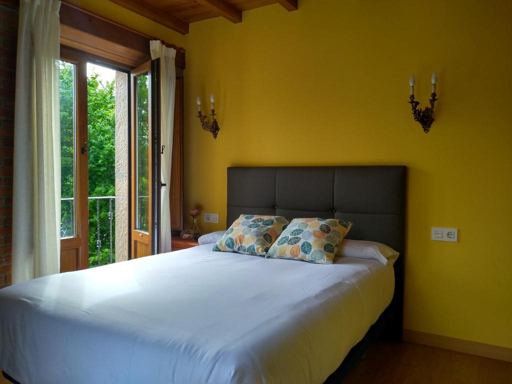 a bedroom with a large bed with yellow walls and a window at Casa de Aldea La Xunta in Cangas de Onís