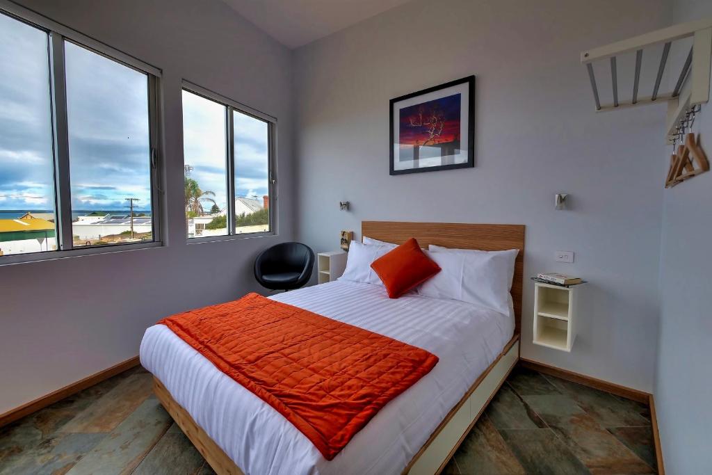 a bedroom with a bed with orange sheets and windows at Cloudscape Apartment No 2 in Kingscote