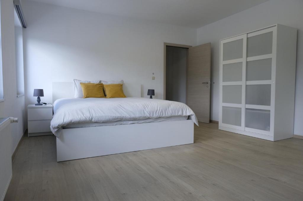 a white bedroom with a large white bed with yellow pillows at Appartement Jemeppe-Bierset-Liège in Liège