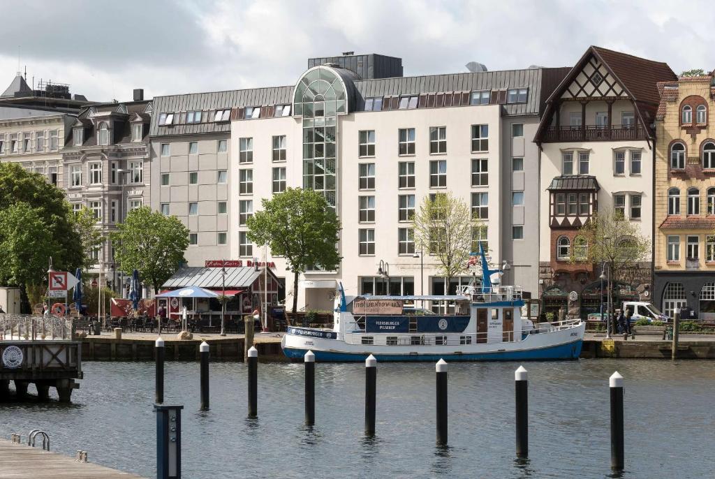 ein Boot im Wasser vor einem Gebäude in der Unterkunft Ramada by Wyndham Flensburg in Flensburg