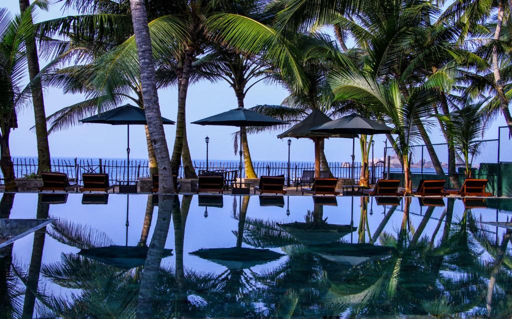 einen Pool mit Stühlen, Sonnenschirmen und Palmen in der Unterkunft Hikka Sandy Pearl Beach Resort in Hikkaduwa