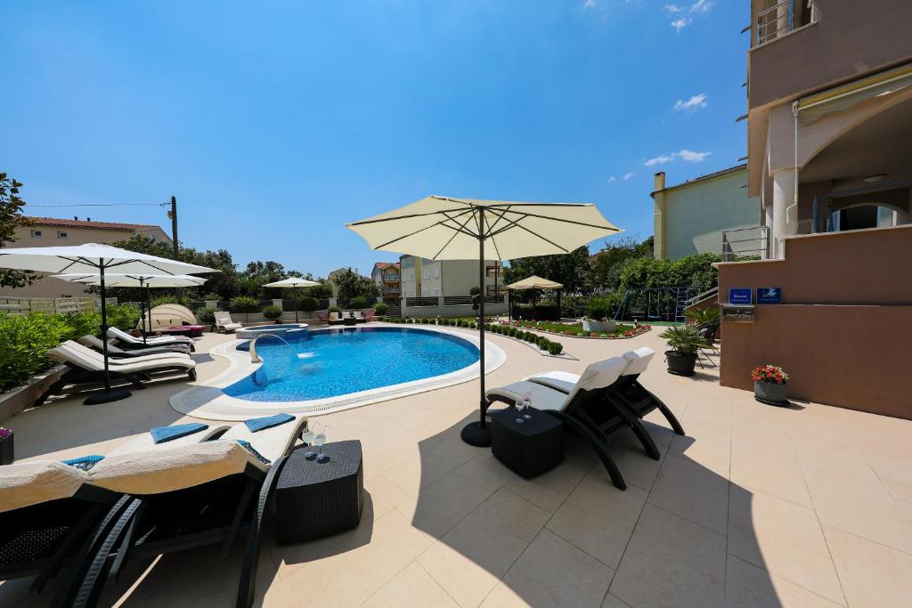 a pool with chairs and an umbrella next to a building at Apartments Tony in Biograd na Moru