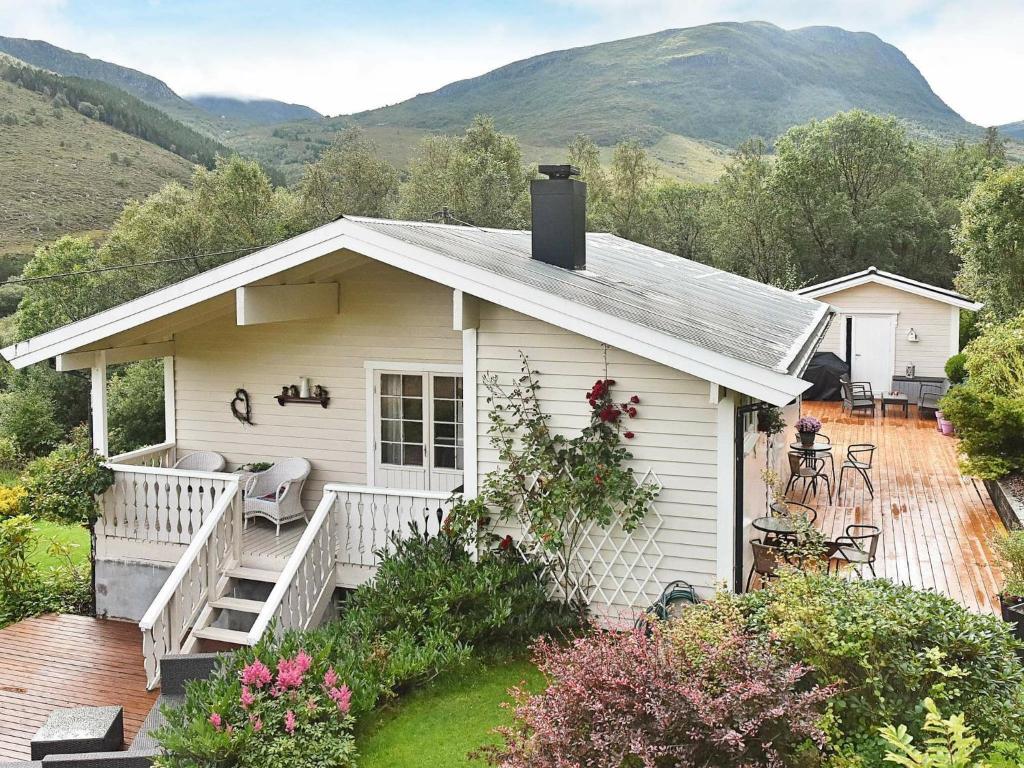 une petite maison blanche avec une terrasse couverte et des montagnes en arrière-plan dans l'établissement Three-Bedroom Holiday home in Åram 1, à Sandvik