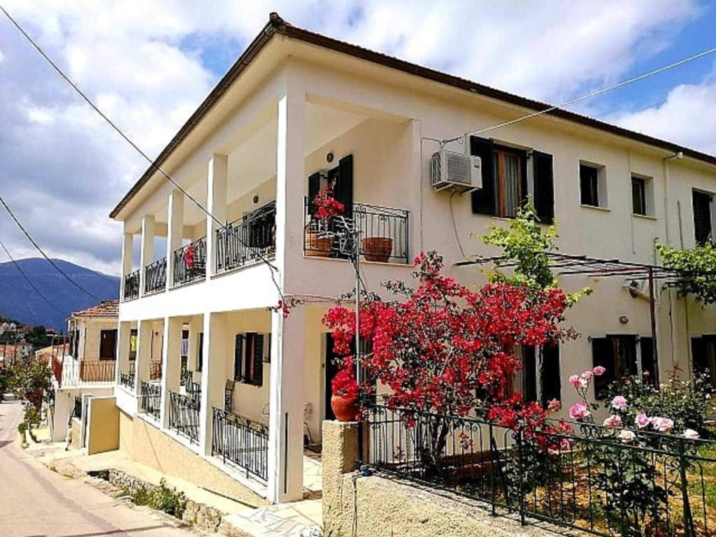 une maison blanche avec des fleurs rouges devant elle dans l'établissement ESTIA HOLIDAY HOUSE, à Vathi