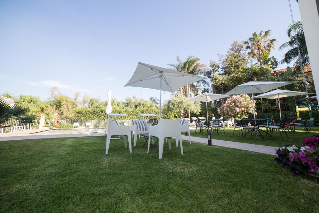 a group of white chairs and umbrellas on a lawn at Sicilia's Art Hotel & Spa in Acitrezza
