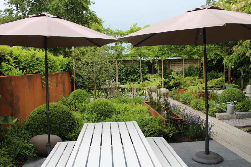 a garden with two white benches and two umbrellas at Bed and garden in Knokke-Heist