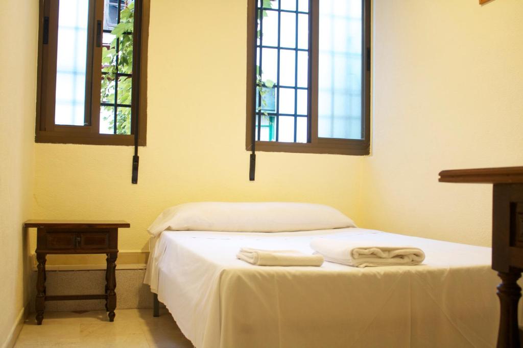 Habitación con 1 cama con sábanas blancas y 2 ventanas. en Hostal Bocanegra, en Granada