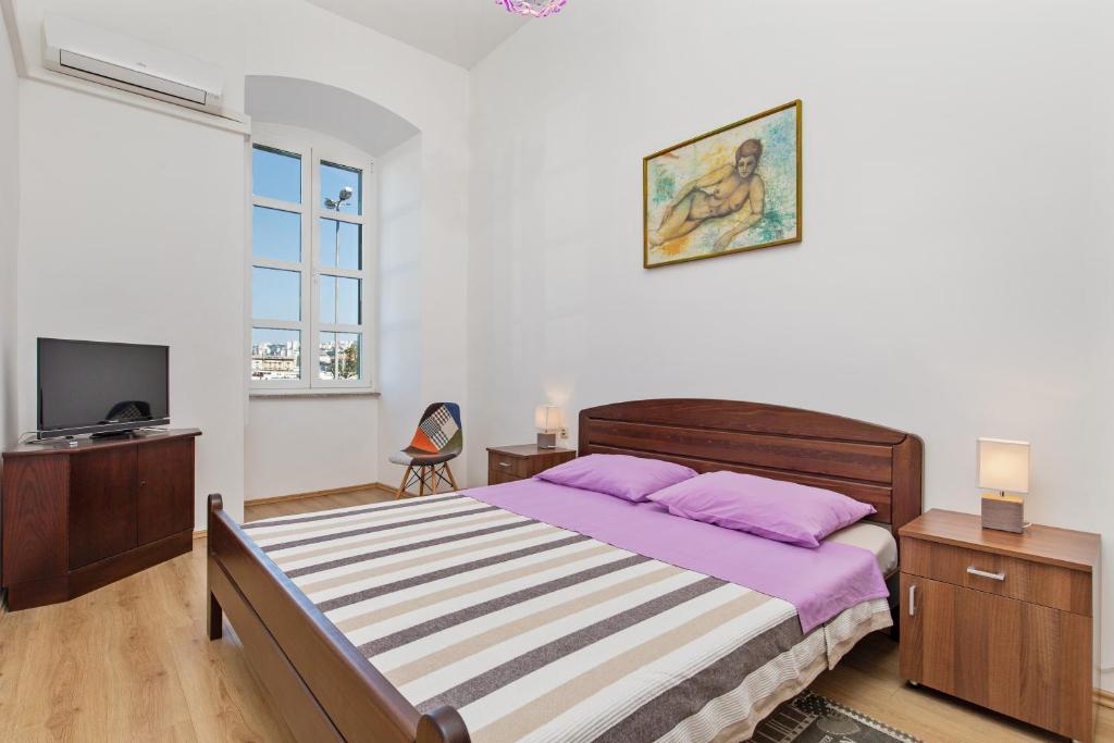 a bedroom with a bed with purple pillows and a tv at Apartment Mia in Rijeka