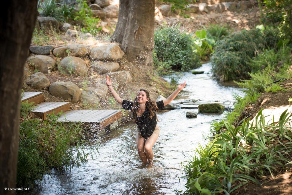 a woman walking through a river with her arms in the air at Brush and Wind in Hagoshrim