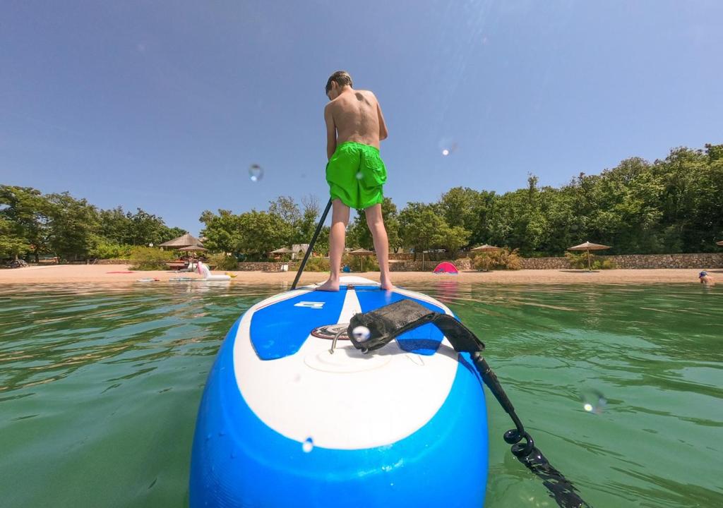 a man is standing on a paddle board on the water at Krk Mobile Homes in Klimno