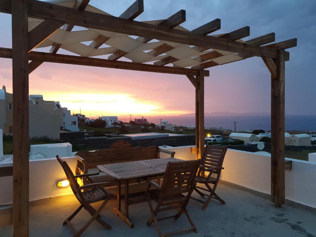 a wooden table and chairs on a balcony with a sunset at Ianthe Apartments & Villa in Oia