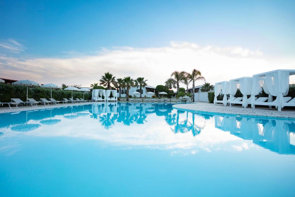 uma grande piscina com cadeiras brancas e palmeiras em Borgo Mulino a Vento - Resort em Uggiano la Chiesa