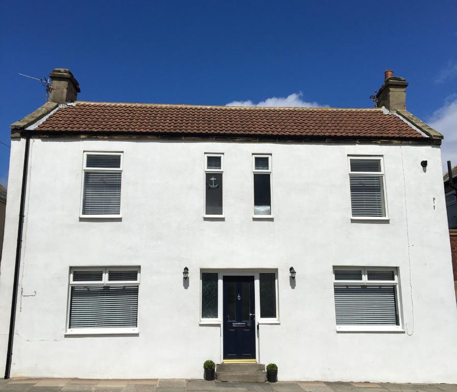 una casa blanca con una puerta azul en Last Cottage en Newbiggin-by-the-Sea