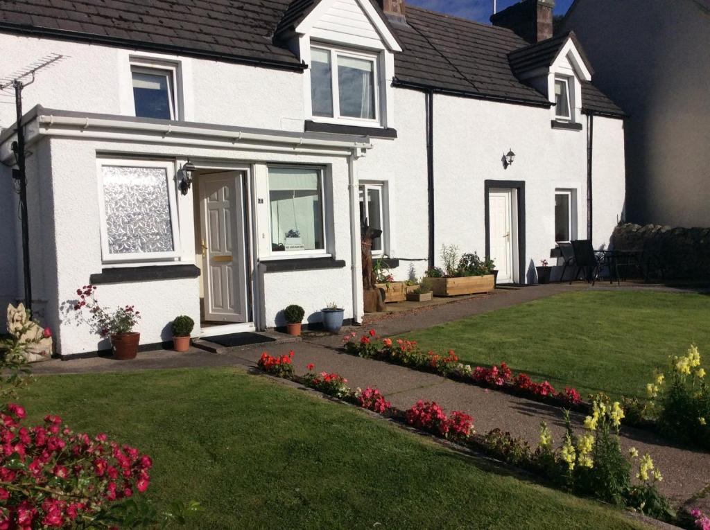 a white house with a yard with flowers at 28 Hillside in Lochinver