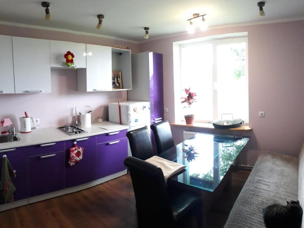 kuchnia z fioletowymi szafkami, stołem i oknem w obiekcie Apartment by the sea (5 minute walk) w mieście Tūja