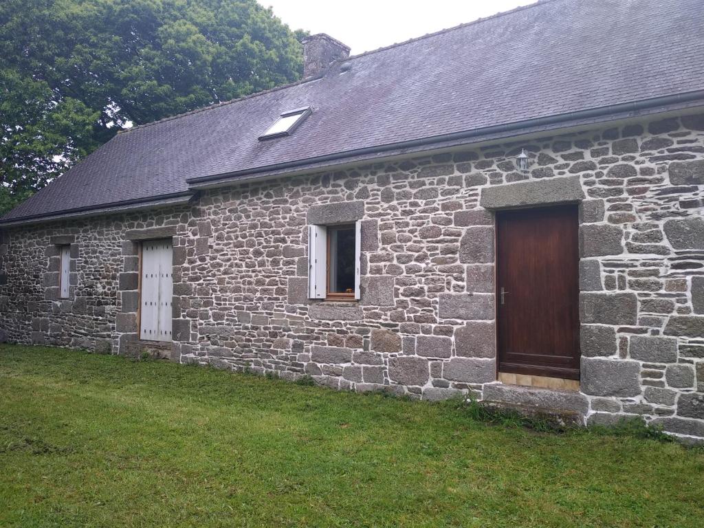 uma casa de pedra com uma porta de madeira e um quintal em Le Botcol em Plouguernével