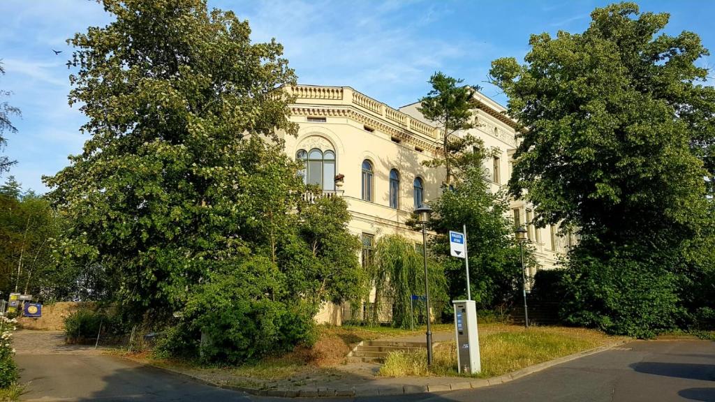 un grand bâtiment blanc avec des arbres devant lui dans l'établissement Stadtvilla An der Viergelindenbrücke, à Rostock