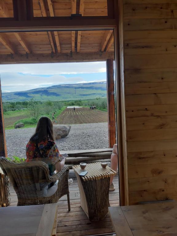 Una donna seduta su una sedia su un portico che guarda fuori da una finestra di Móðir Jörð Organic Farm Guesthouse in Vallanes a Vallanes