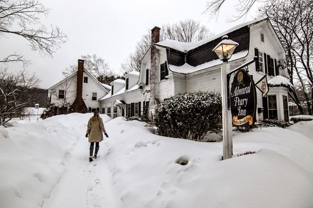 Una mujer caminando por una calle cubierta de nieve delante de una casa en Admiral Peary Inn, en Fryeburg