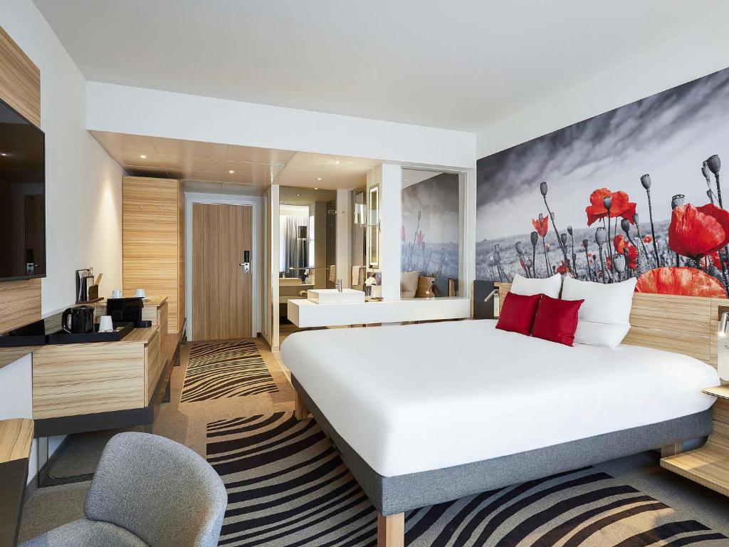 
a hotel room with a bed, chair, and a painting on the wall at Novotel Ieper Centrum in Ieper
