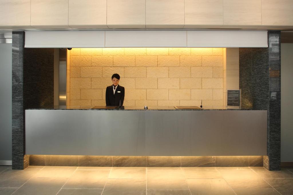 a man in a suit standing behind a counter at Tokyu Stay Kamata - Tokyo Haneda in Tokyo