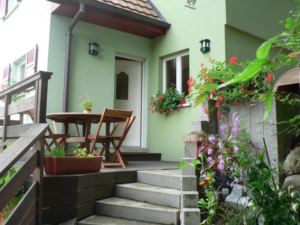 Cette petite maison dispose d'une terrasse couverte avec une table et des fleurs. dans l'établissement Gite de la Lisière du Bois, à Ueberstrass