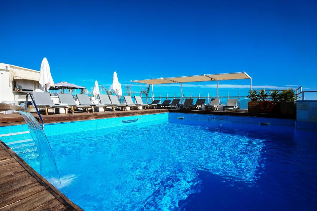a swimming pool with chairs and the ocean in the background at Capsis Astoria Heraklion in Heraklio Town