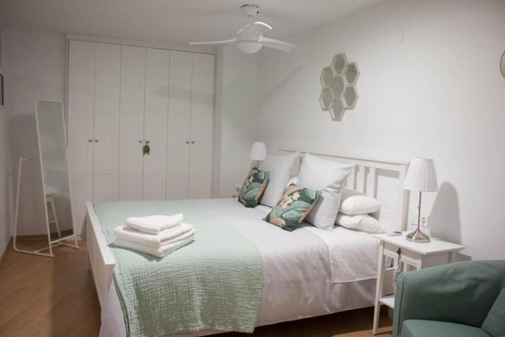 a white bedroom with a bed and a green chair at Apartamento Reyes Catolicos in Almería