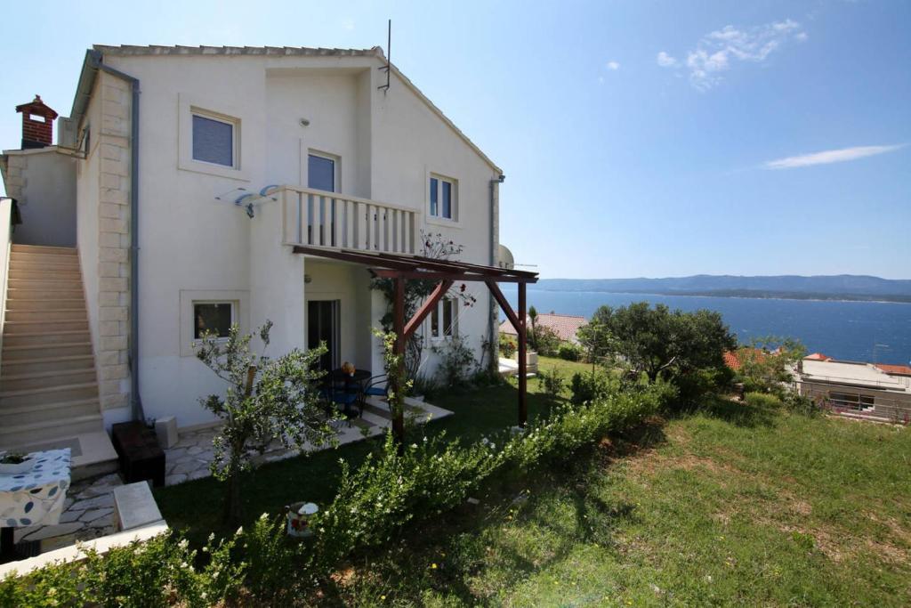 a white house with a balcony and the water at Apartmani Villa Panorama in Bol