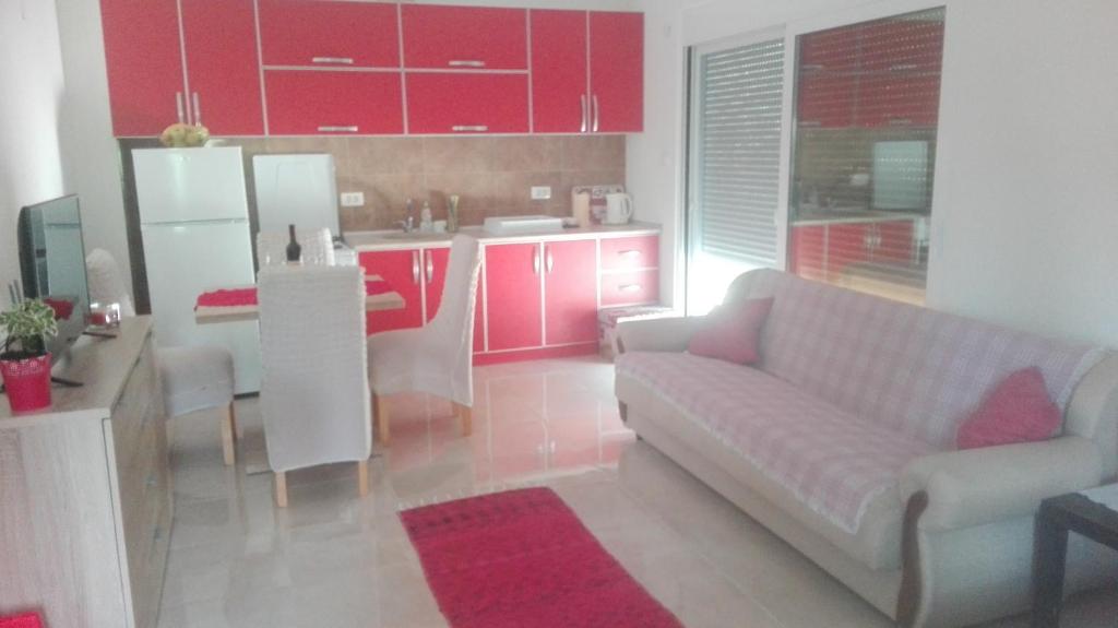 a living room with a couch and a kitchen with red cabinets at Apartman Strahinja in Tivat