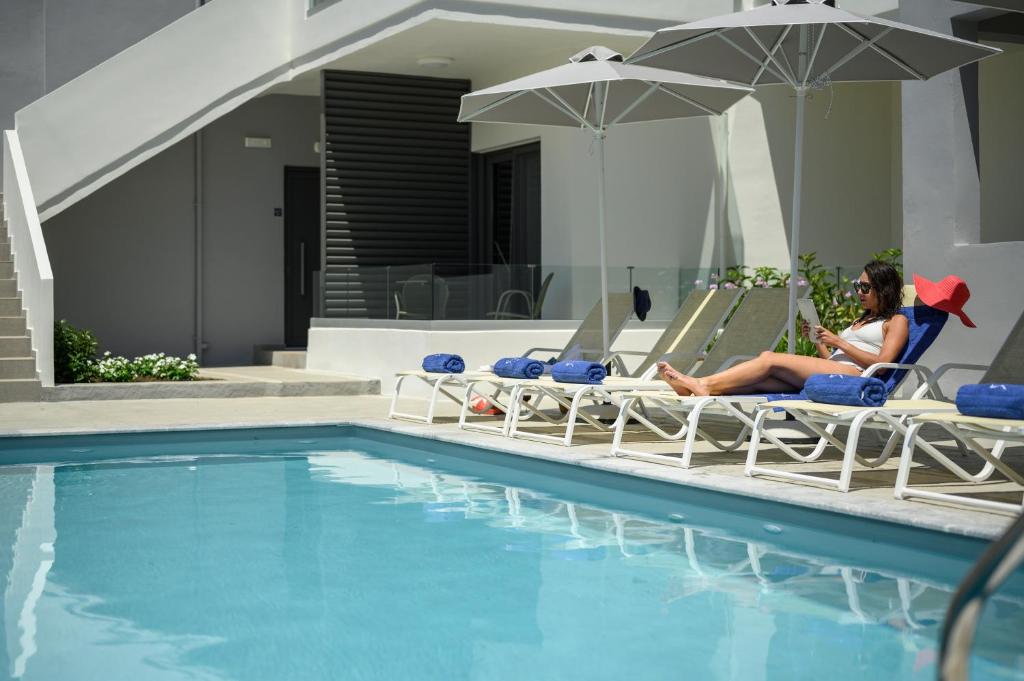 a woman sitting in lawn chairs next to a swimming pool at Athina Suites Luxury Suites Near The Sea Platanias in Platanias