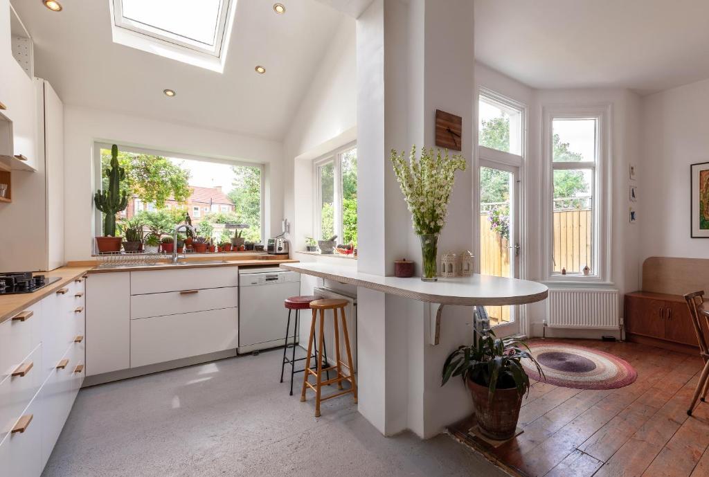 een keuken met witte kasten en een tafel en ramen bij Veeve - Duckett's Green Charm in Londen