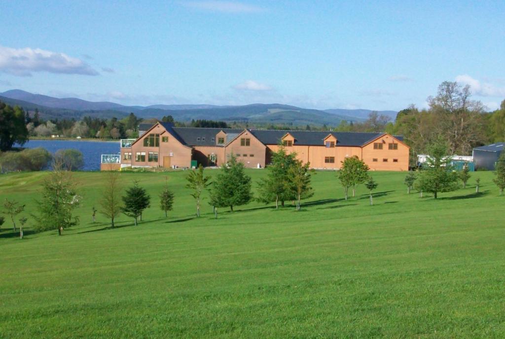 a large grassy field with a house and trees at The Lodge on the Loch in Aboyne