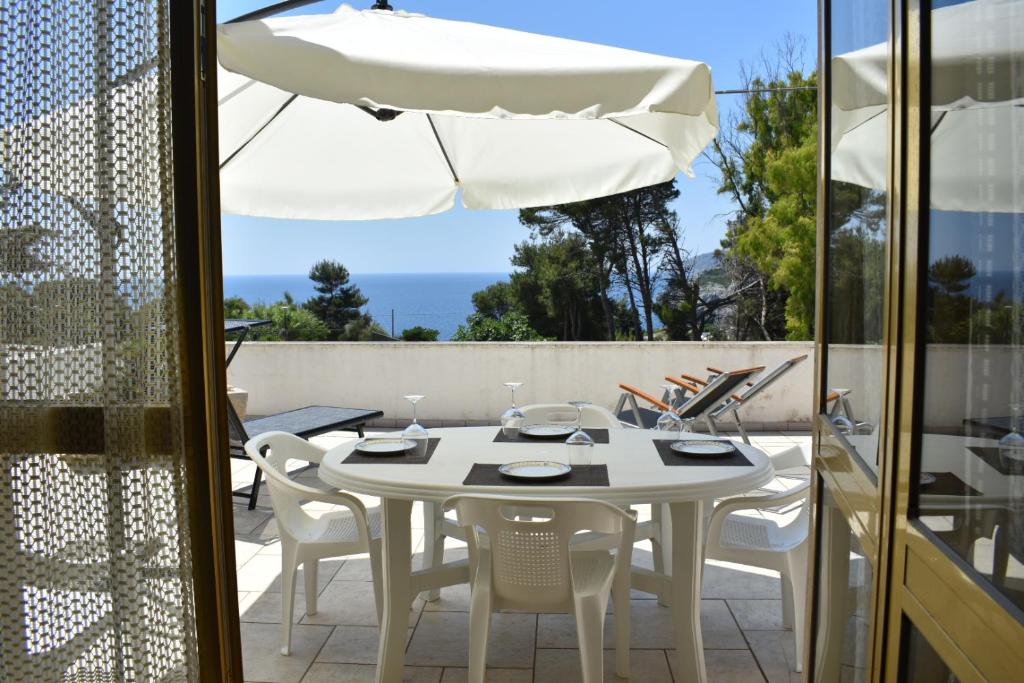 una mesa blanca con sillas y una sombrilla en el patio en La terrazza sul mare - Marina di Novaglie, en Alessano