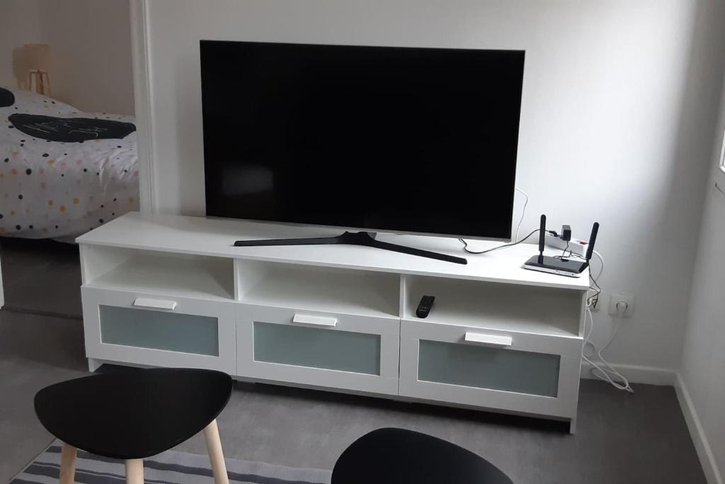 un televisor sentado en una cómoda blanca con dos sillas en Elbeuf Etage 1 sweet home Netflix wifi, en Elbeuf