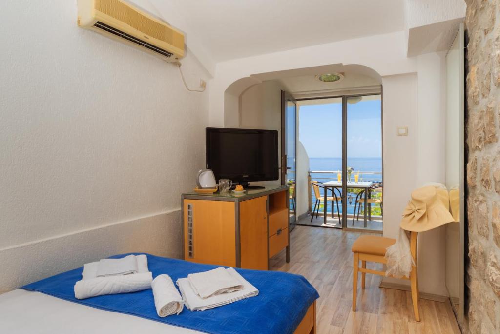 a room with a bed and a television and a balcony at Hotel Savojo in Petrovac na Moru