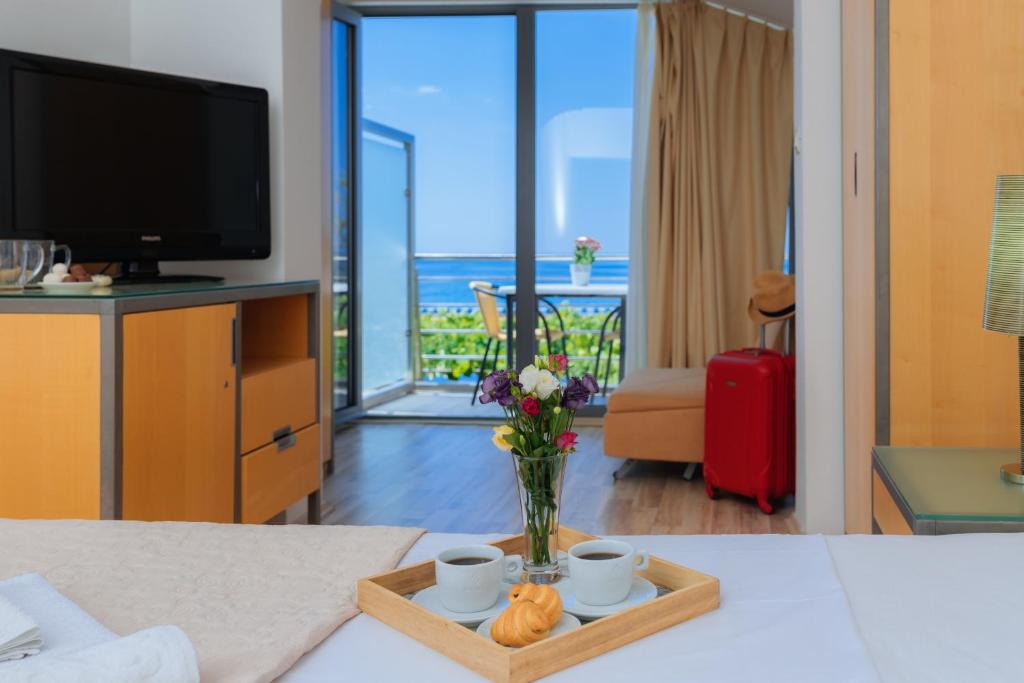 a living room with a television and a table with a vase of flowers at Hotel Savojo in Petrovac na Moru