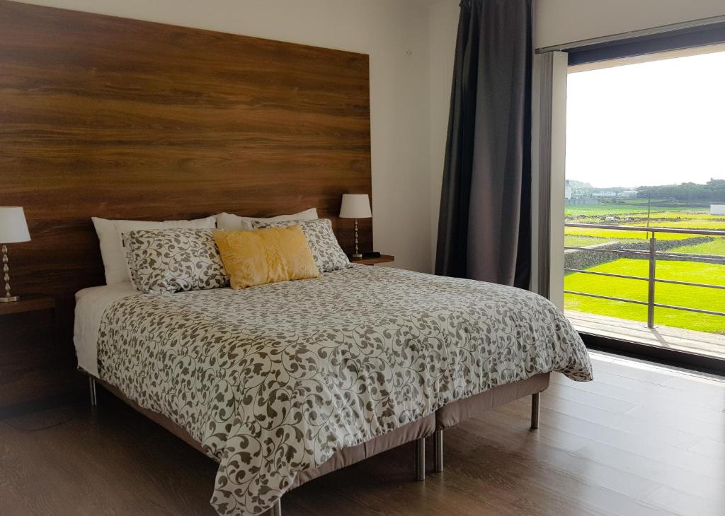 1 dormitorio con 1 cama con cabecero de madera y ventana en Casa Milhafre, en Praia da Vitória
