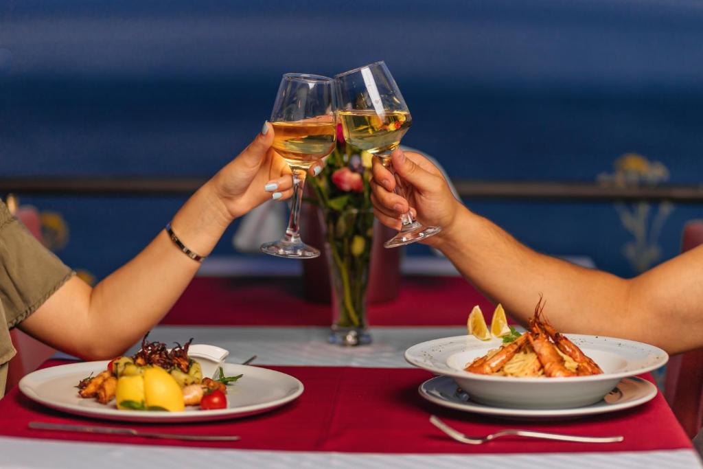 two people holding up glasses of wine at a table with food at Hotel Savojo in Petrovac na Moru
