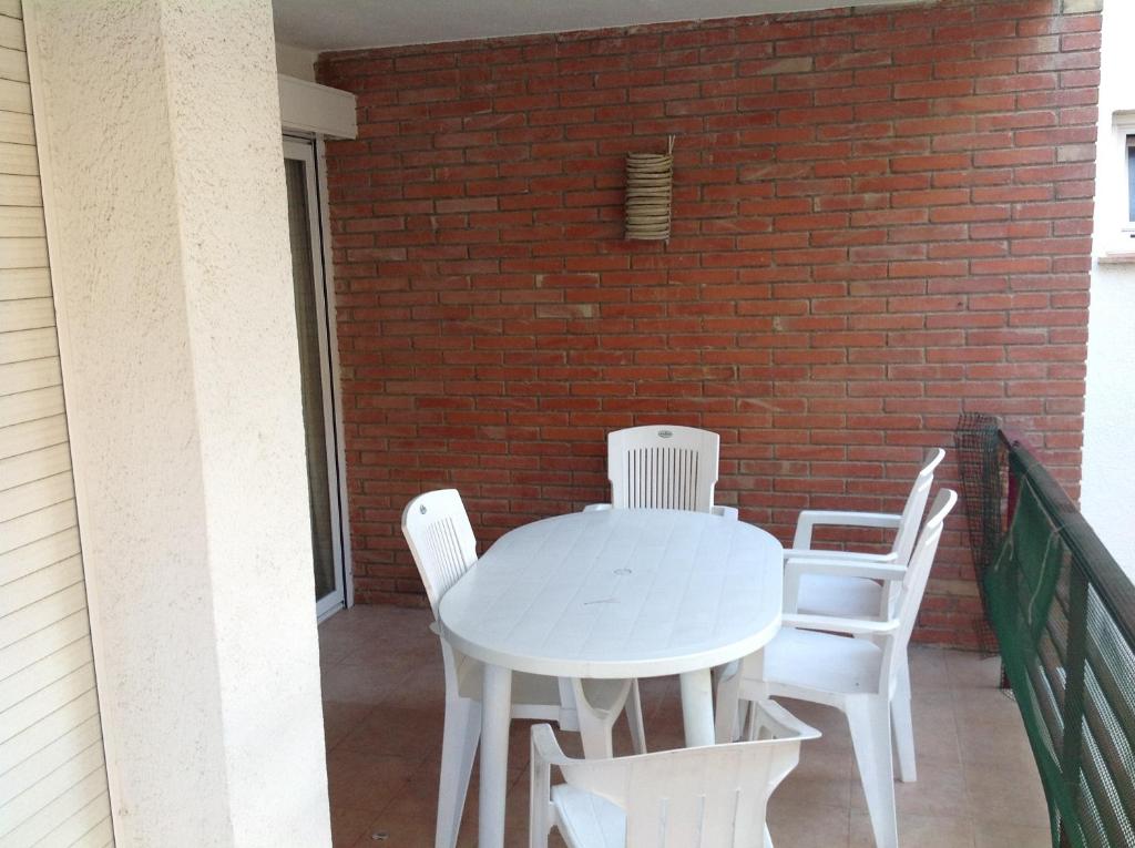 una mesa blanca y sillas en un balcón con una pared de ladrillo en Apartament Turístic Alhambra, en Platja d'Aro